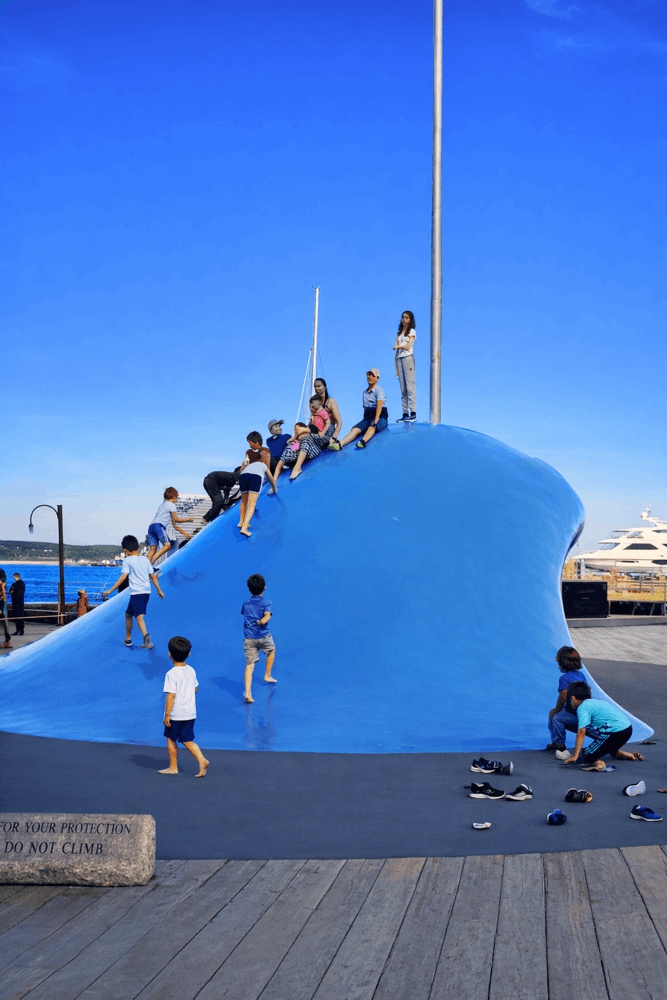 Children climbing the large blue Wave sculpture on the Halifax Waterfront boardwalk